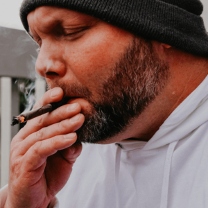 a man in a hoodie smoking a brown blunt