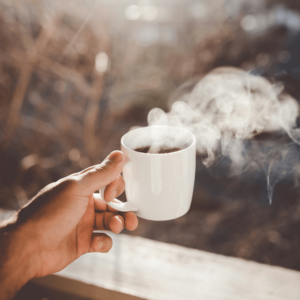 person holding a steaming white mug of coffee