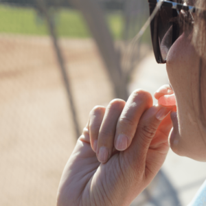 girl in sunglasses taking a pink gummy