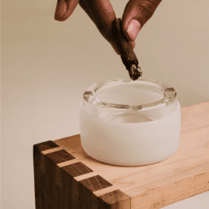 a hand holding a cigar over a glass ashtray