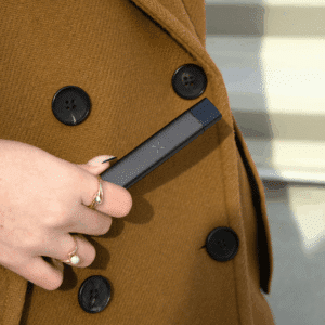 person in pea coat holding a vape pen